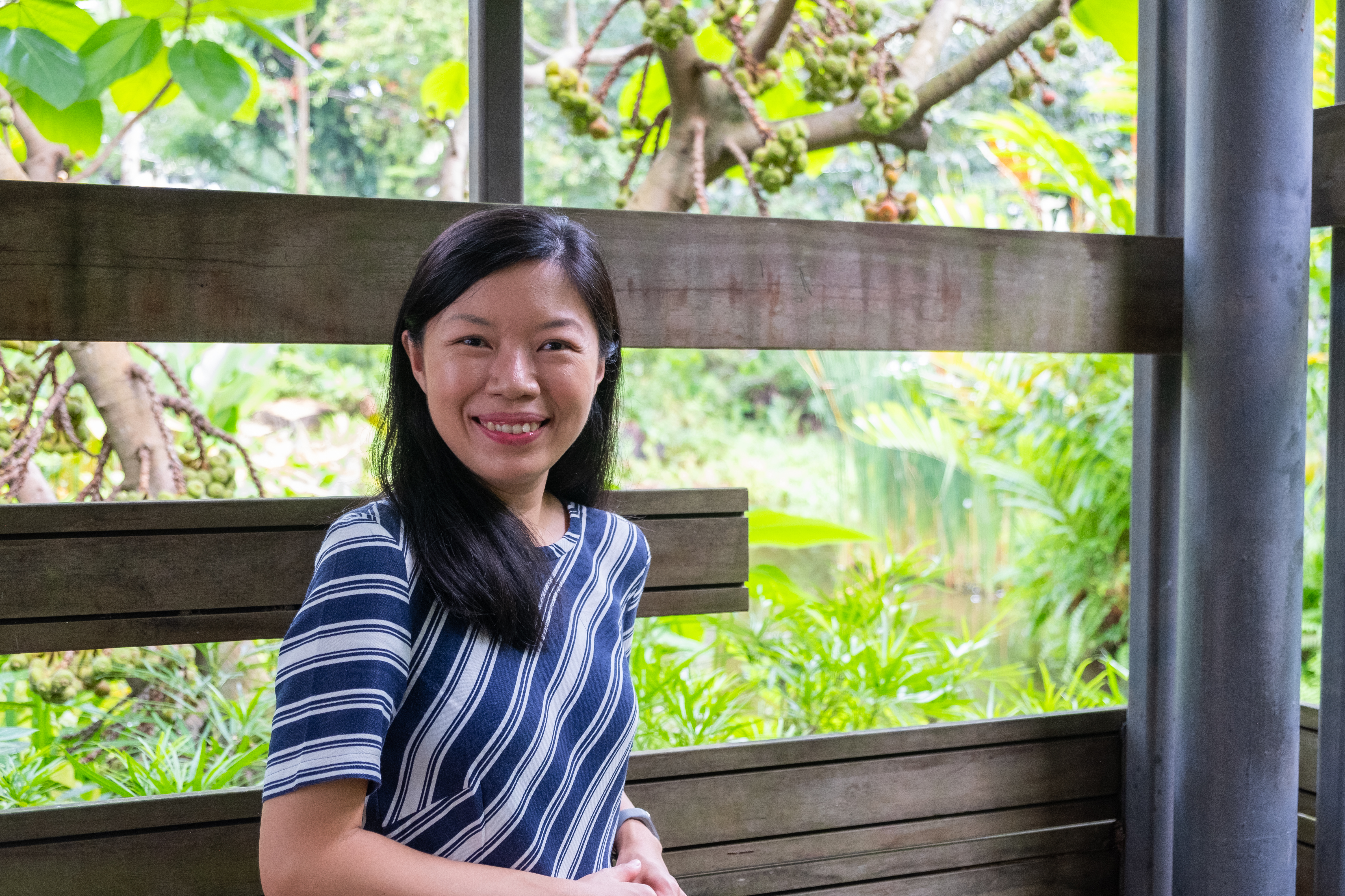 Sharon smiling warmly at the camera with lush green foliage in the background.