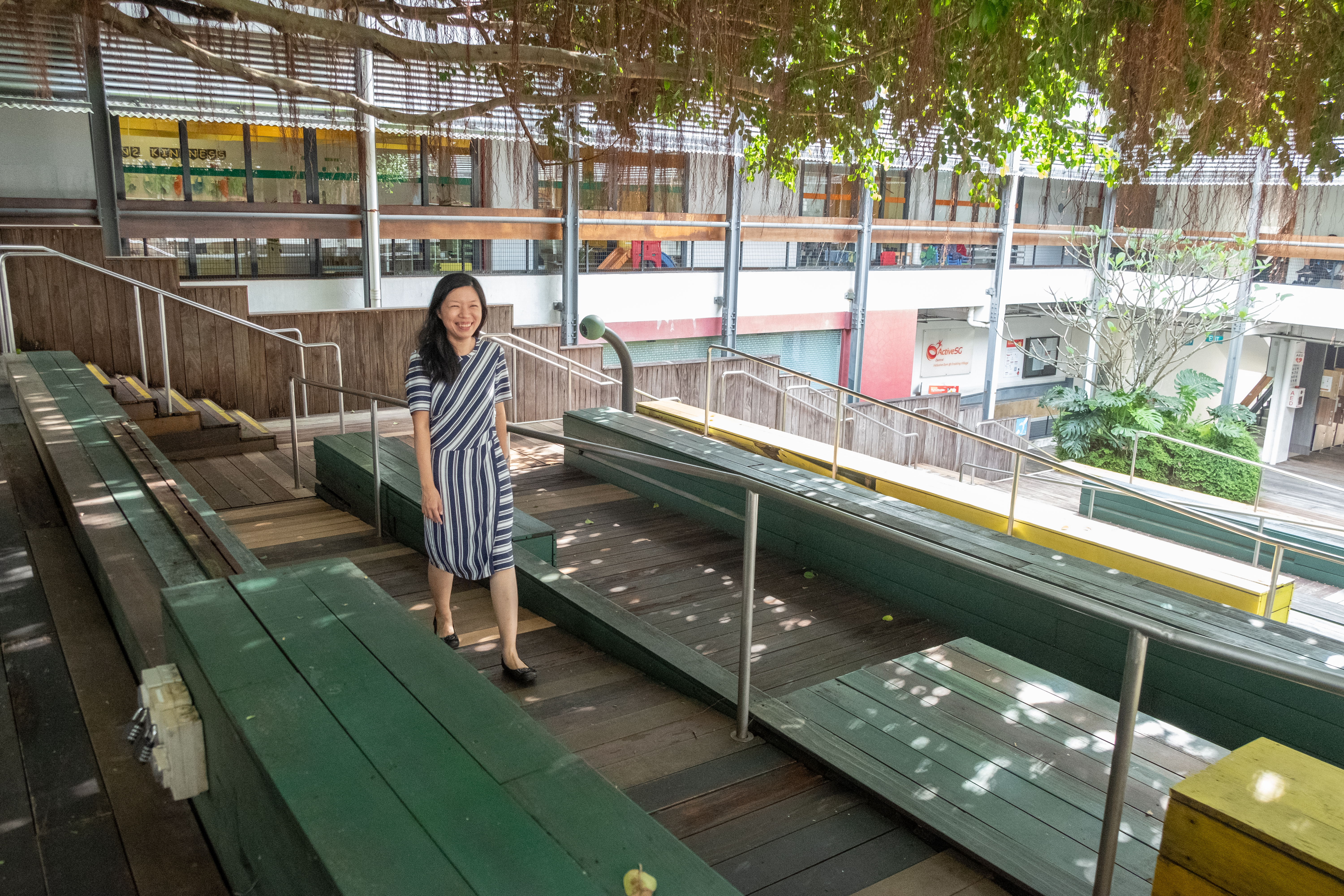 Sharon walking along a wooden pathway with a joyful smile, surrounded by natural scenery and buildings.