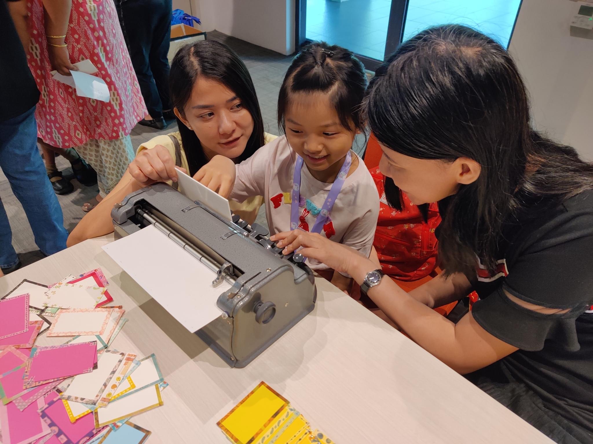  A young girl experimenting with the Perkins Brailler with the help of two volunteers.