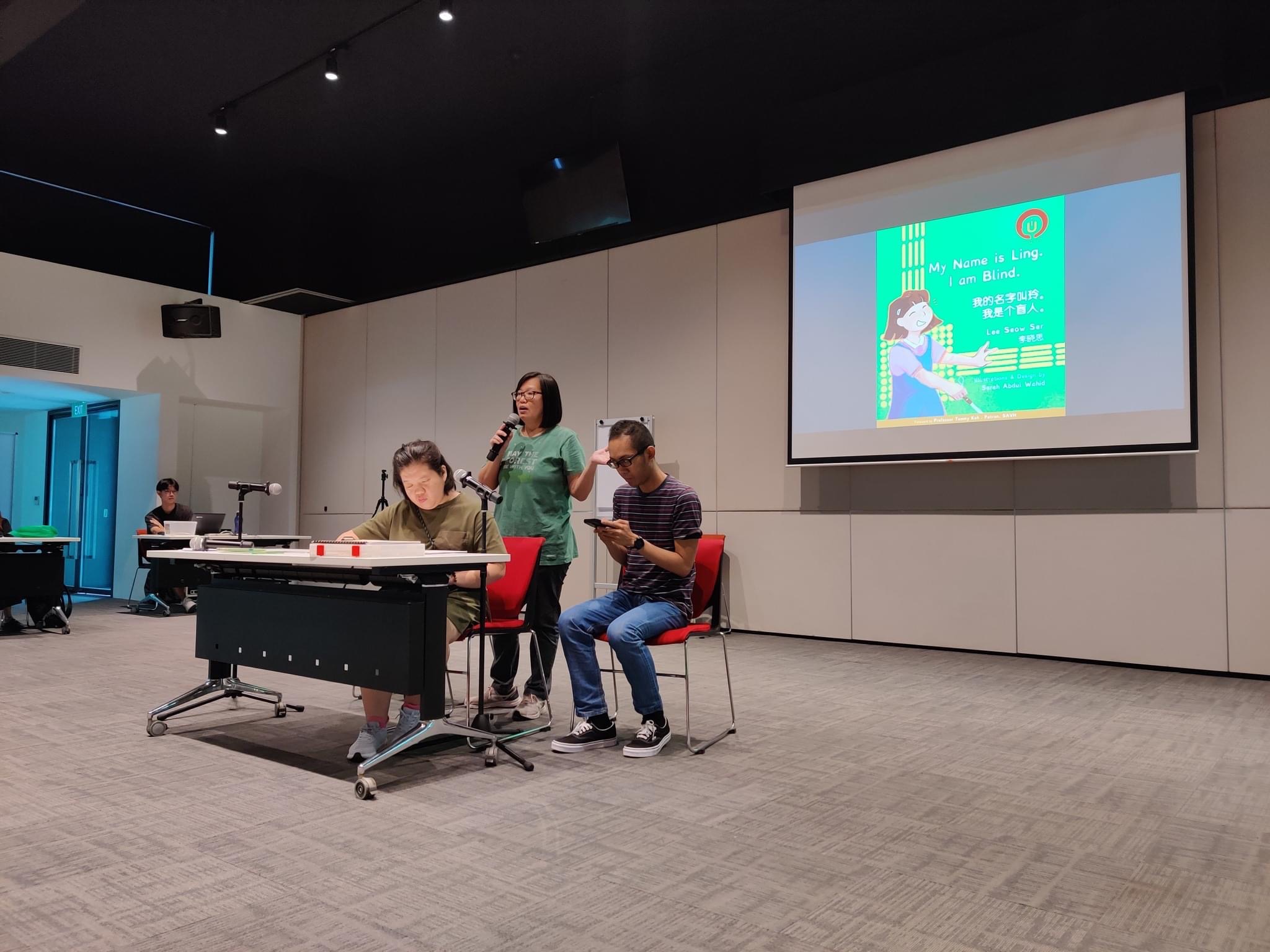 Siew Ling at the front of the Ability Hub reading My Name is Ling. The book cover is projected on the screen behind her.